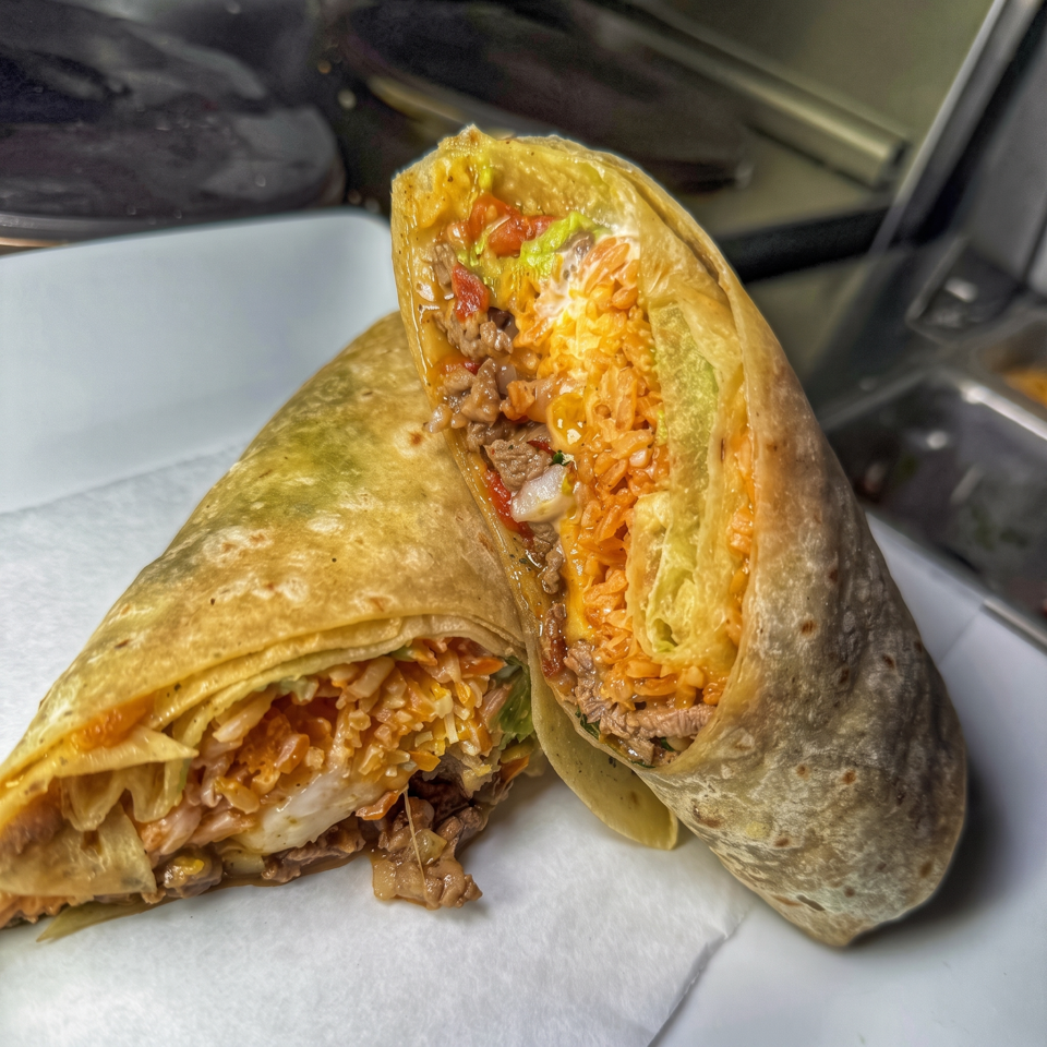 Close-up of a stuffed tortilla wrap filled with seasoned beef, Mexican rice, lettuce, tomatoes, onions, and melted cheese.